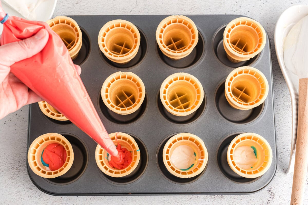 piping red cake batter inside an ice cream cone
