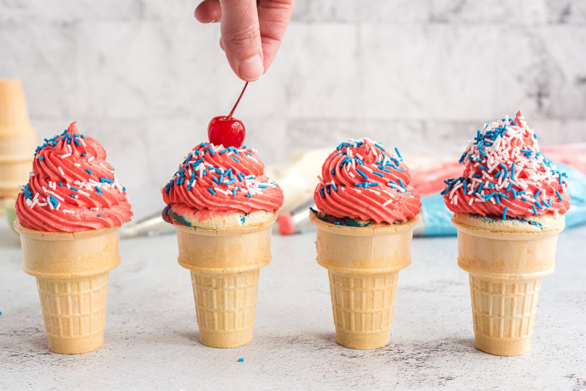 adding maraschino cherry to ice cream cone cupcakes