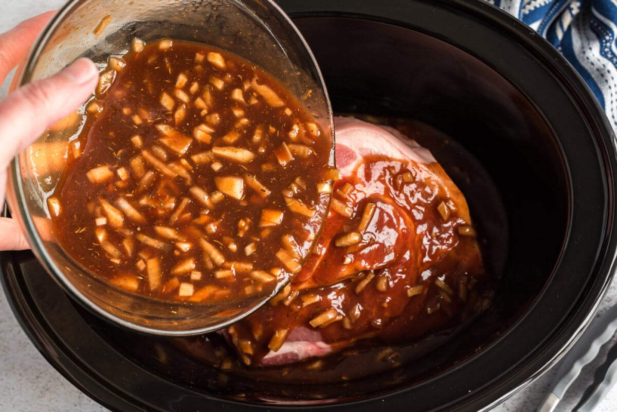 pouring sauce over pulled pork in slow cooker