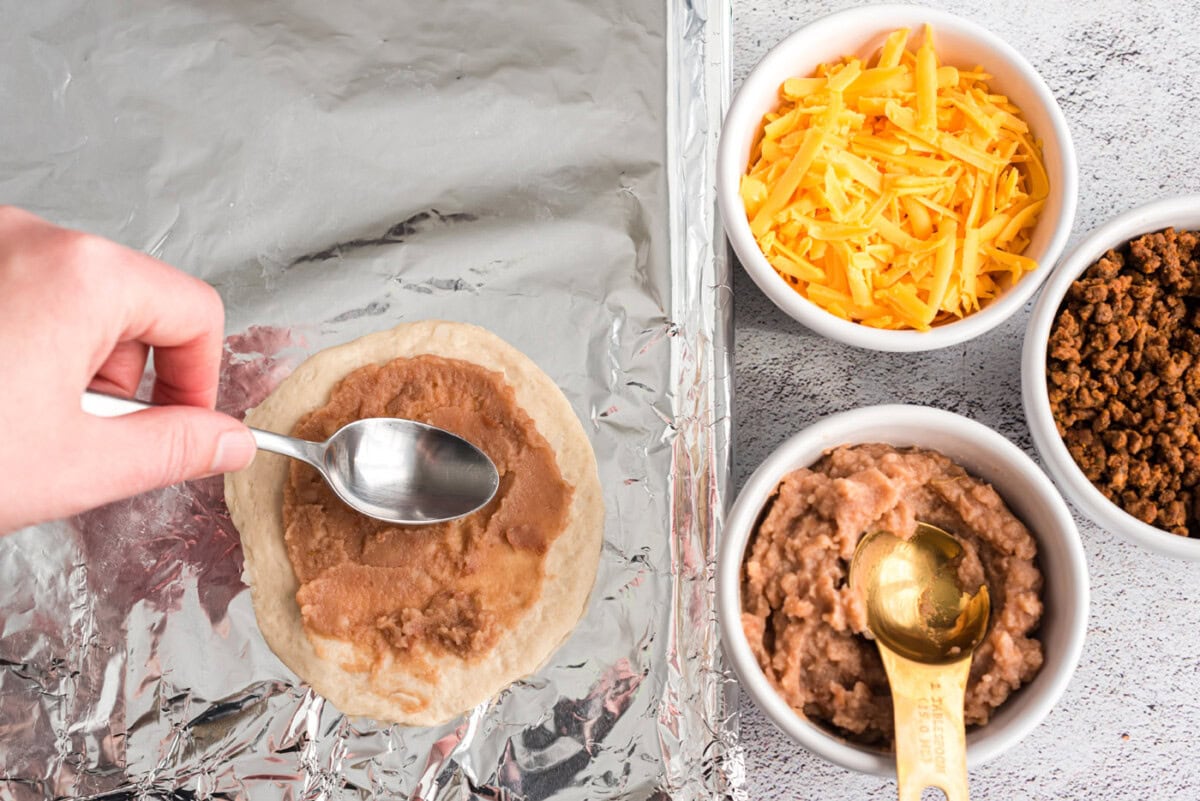 spreading refried beans on biscuit dough