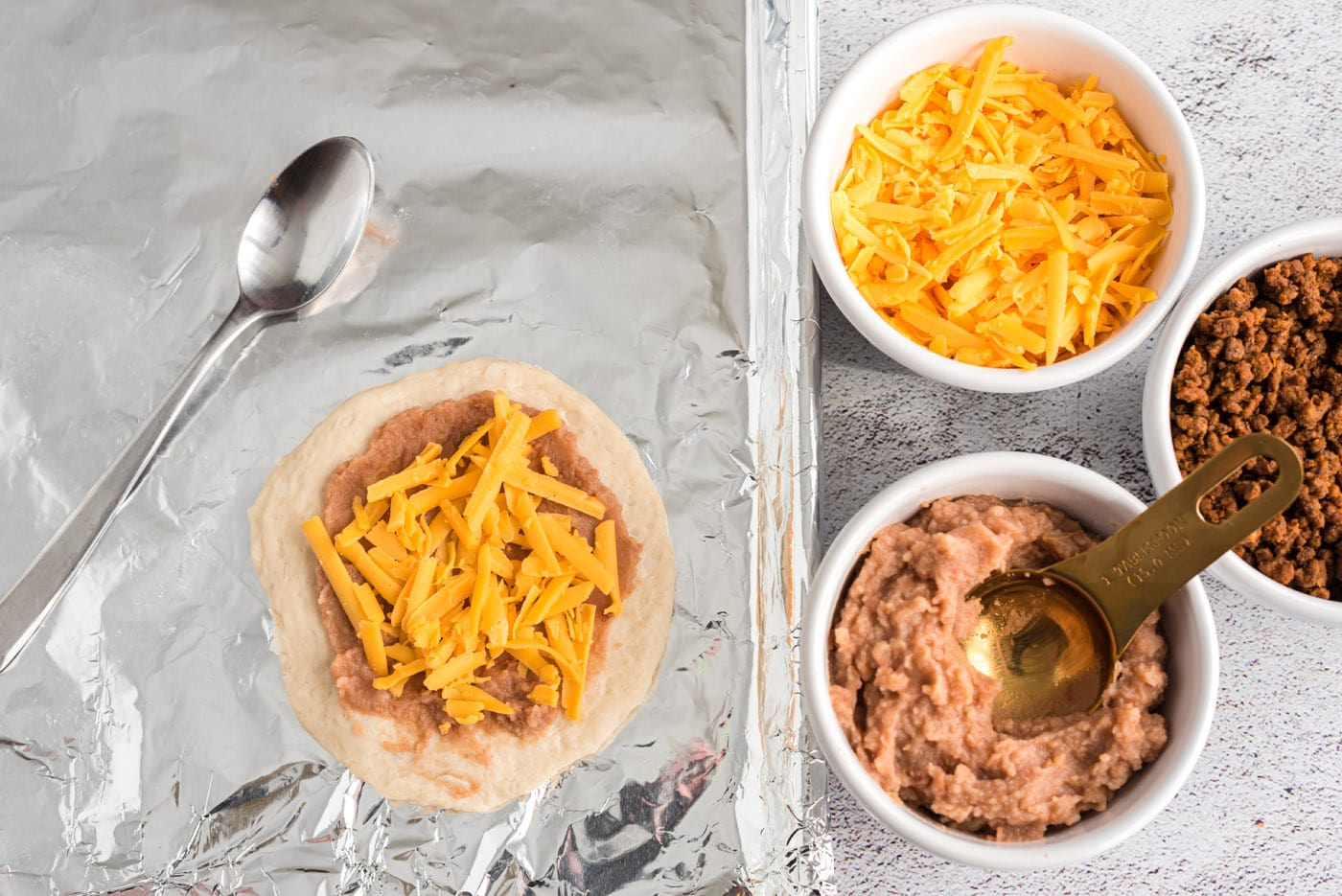 shredded cheese over refried beans and biscuit dough