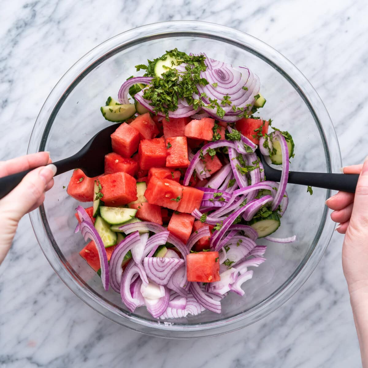 tossing watermelon salad ingredients together in a bowl