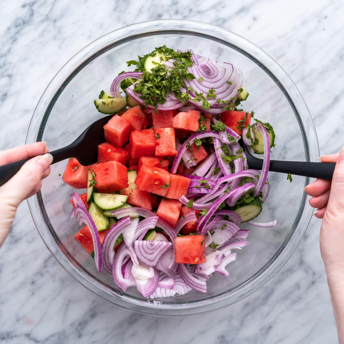 tossing watermelon salad ingredients together in a bowl