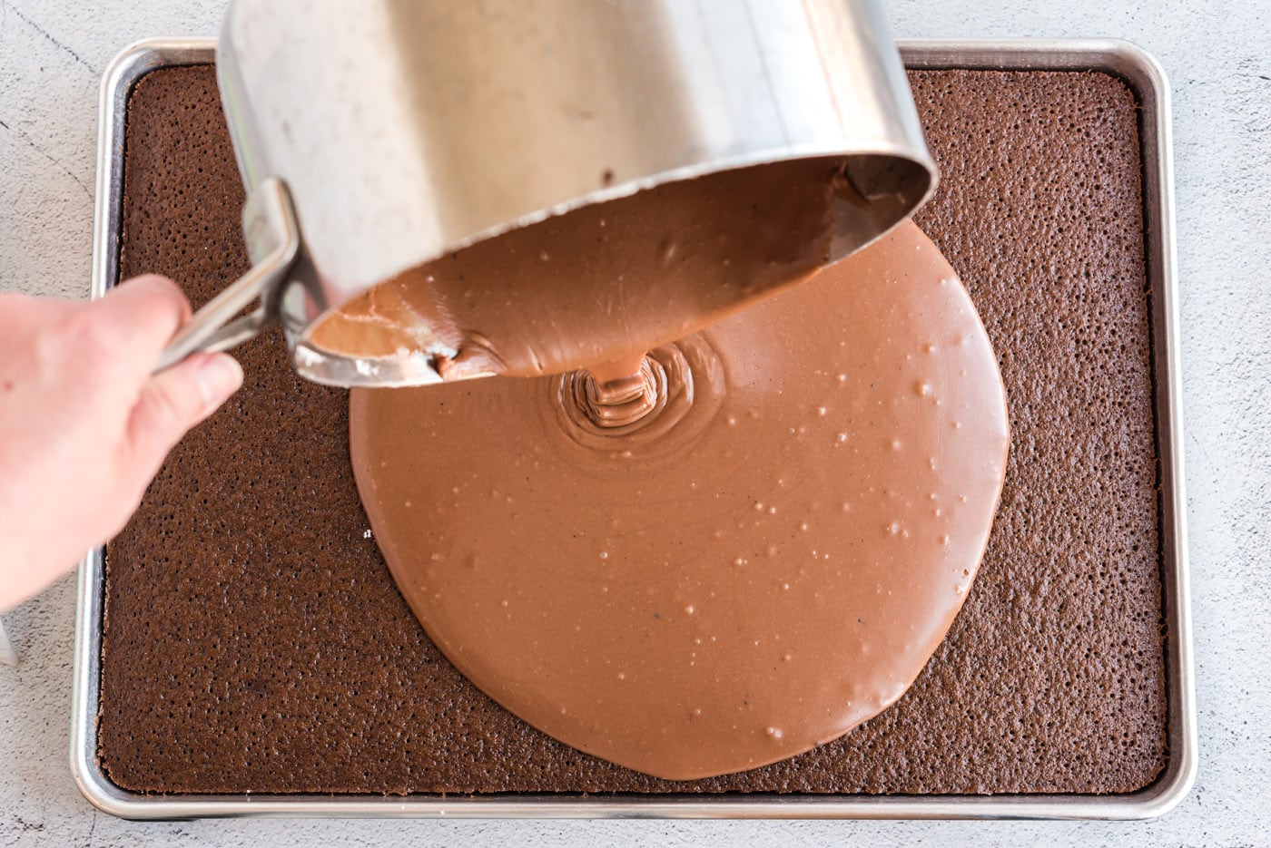 pouring chocolate icing over hot chocolate sheet cake