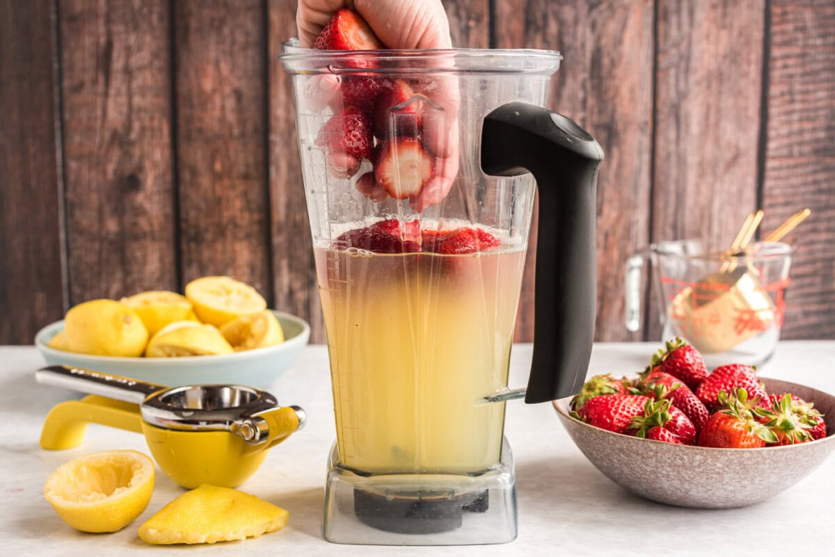 adding strawberries to blender with lemon juice and water