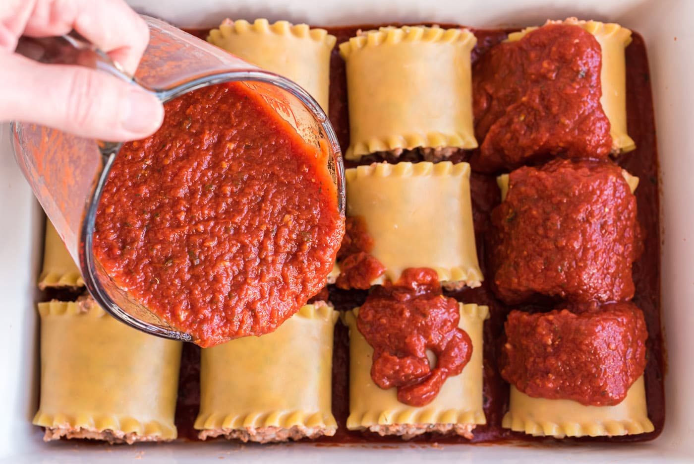 pouring sauce over lasagna roll ups in a dish