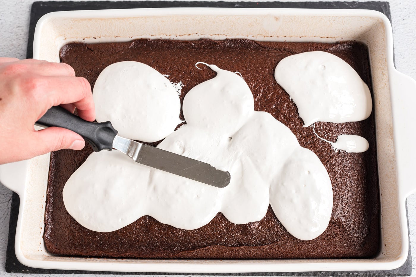 spatula spreading marshmallow cream over coca cola cake