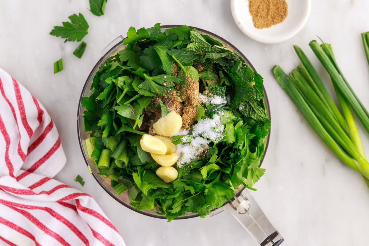 fresh herbs and garlic added to food processor with chickpeas