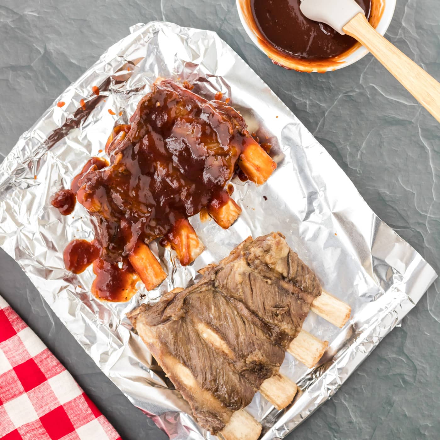 brushing barbecue sauce onto ribs on a baking sheet