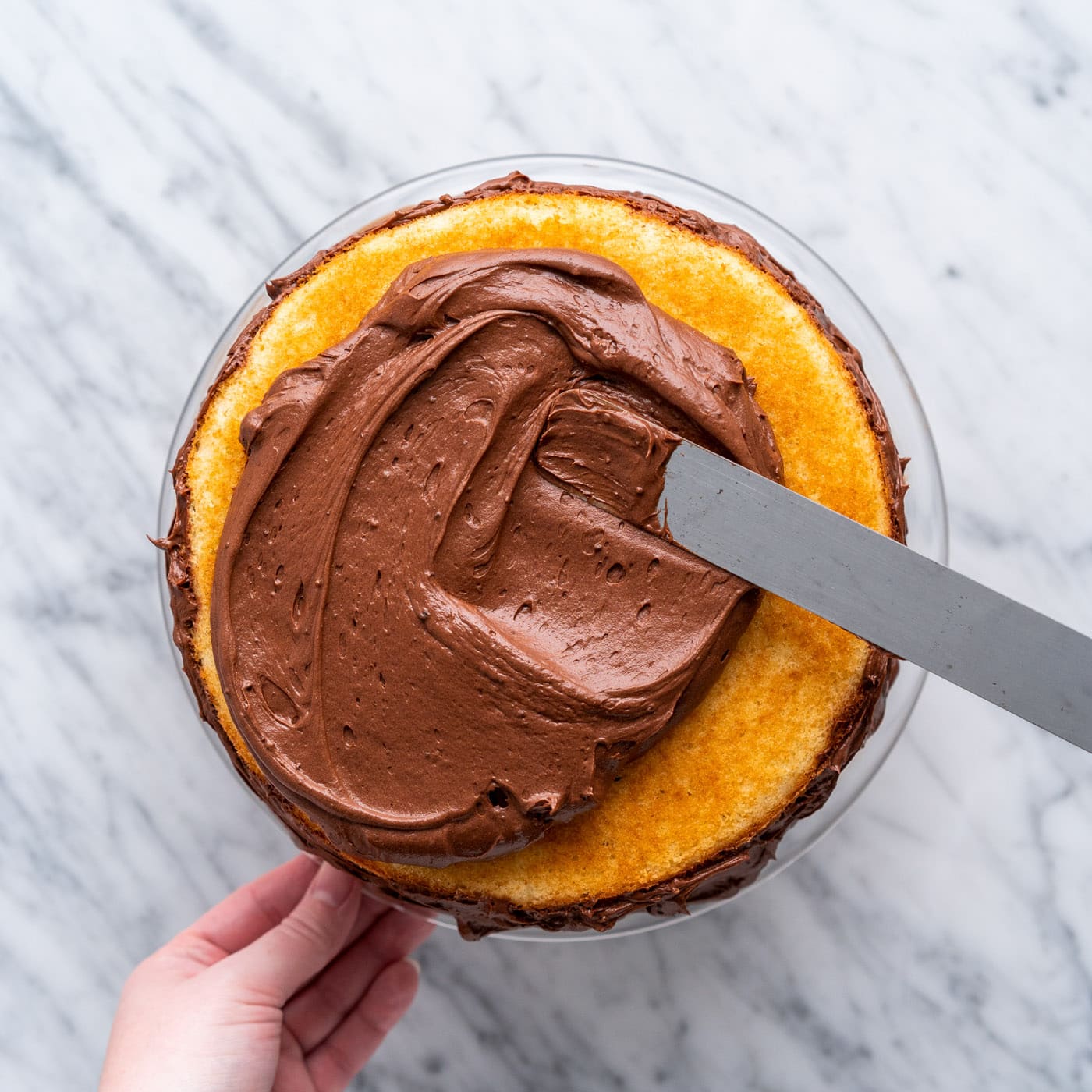 spatula spreading chocolate frosting over yellow marble cake