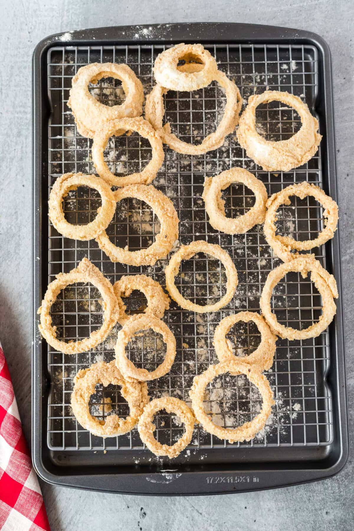 onion rings dipped in breadcrumbs on a baking sheet