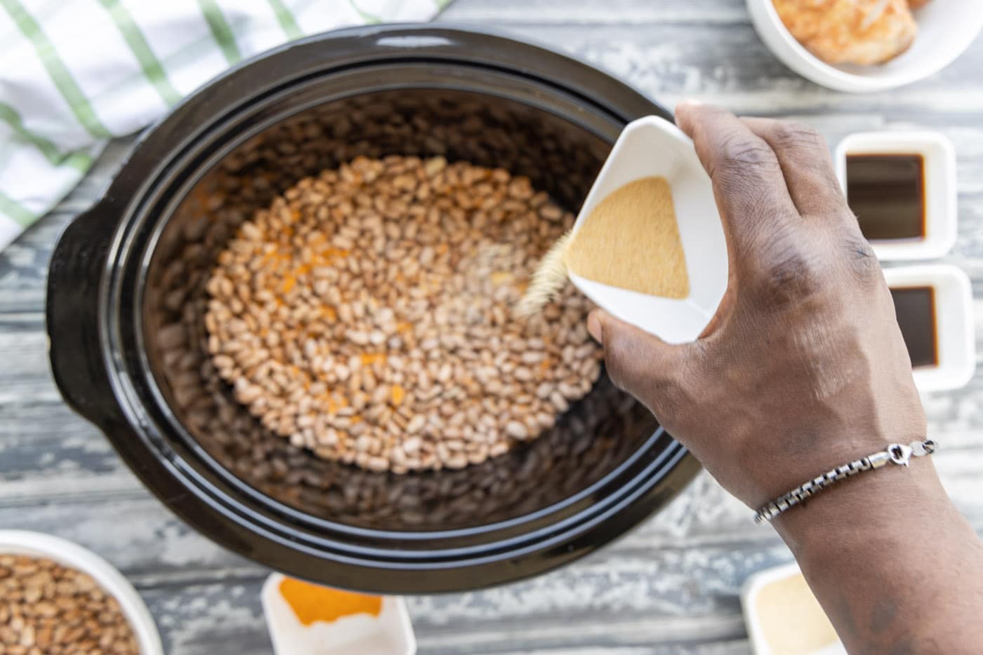 pouring seasoning over pinto beans in a crockpot