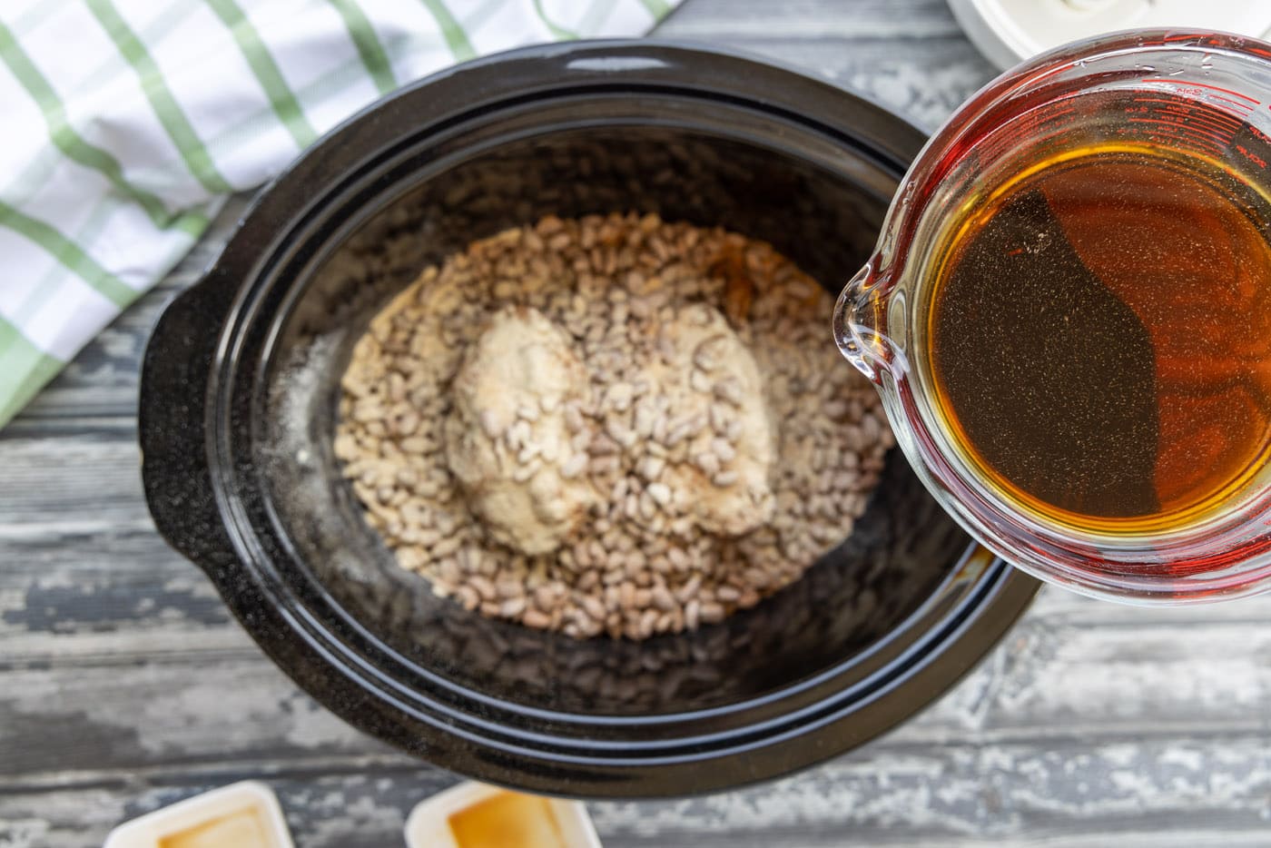 pouring liquid smoke and soy sauce over pinto beans in the crockpot