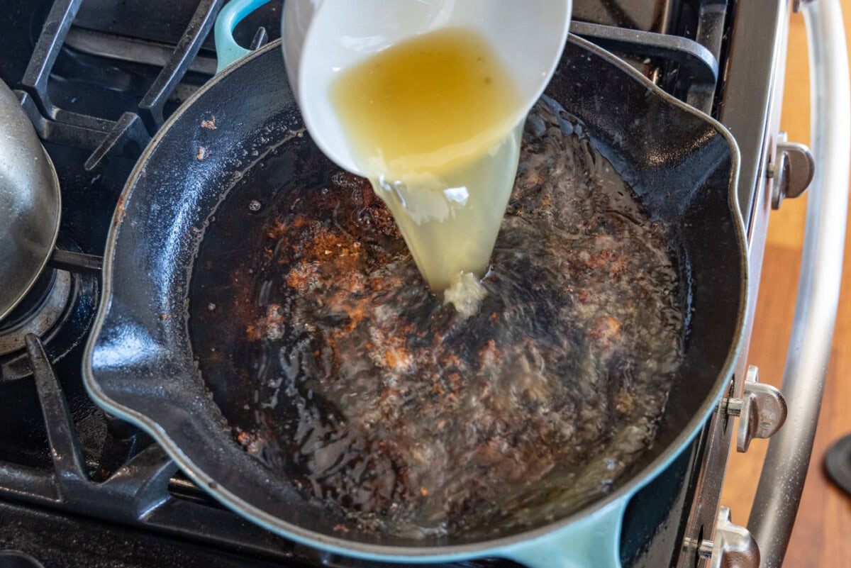 adding chicken broth to skillet