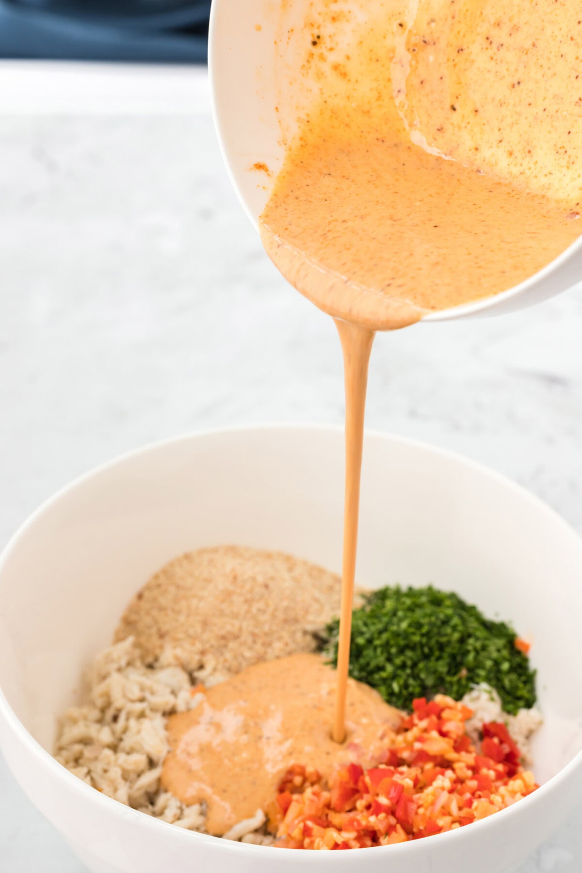 pouring sauce over crab cake mixture in a bowl