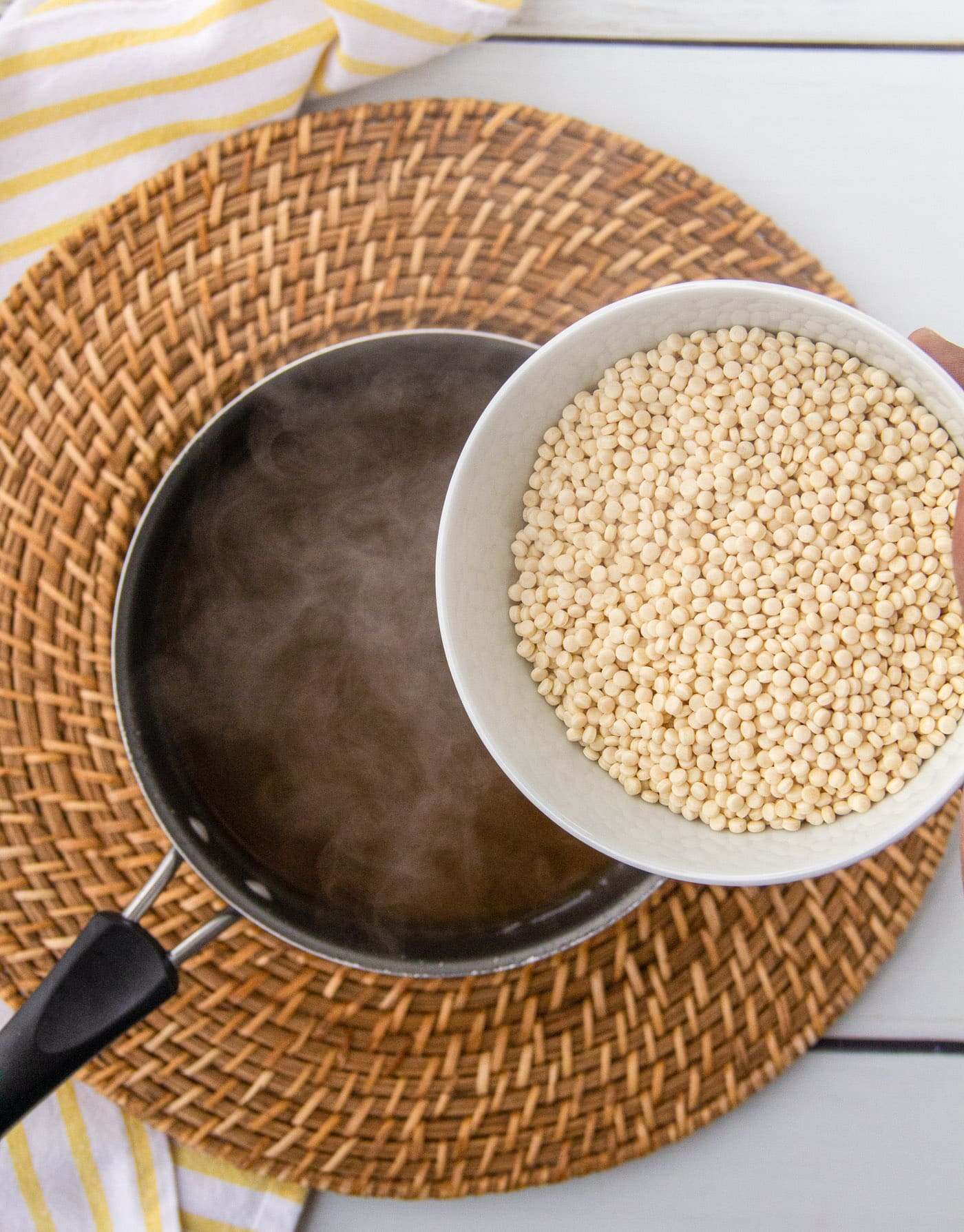 pouring couscous into broth in a saucepan