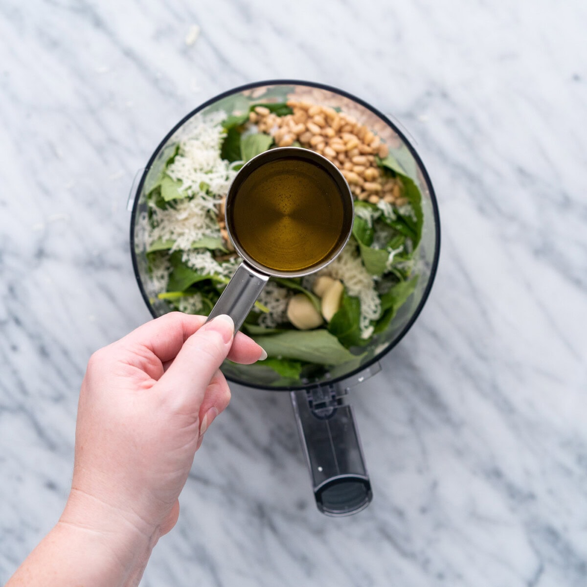 olive oil in a cup over basil pesto ingredients