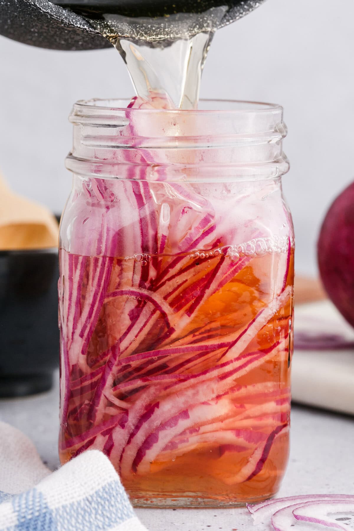 pouring vinegar over sliced red onions in a mason jar