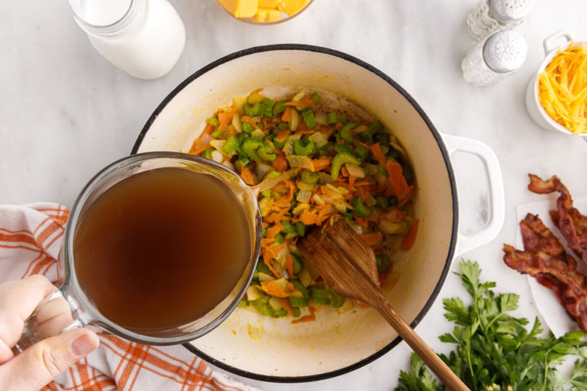 pouring beef broth over vegetables in a stockpot