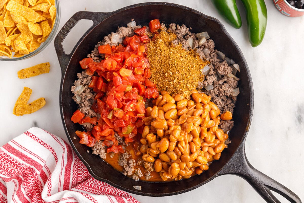 taco seasoning, beans, and tomatoes added to ground beef in a skillet