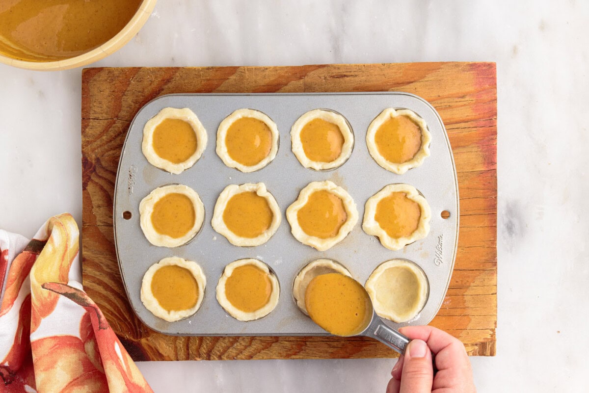 adding pumpkin pie filling to pie dough in muffin pan