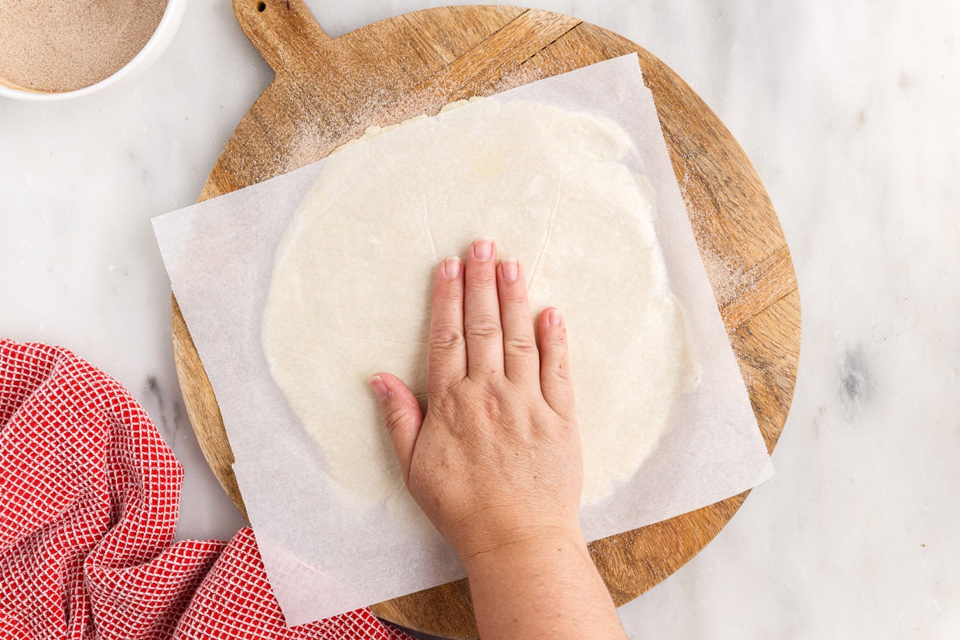 hand on top of dough disc with parchment paper