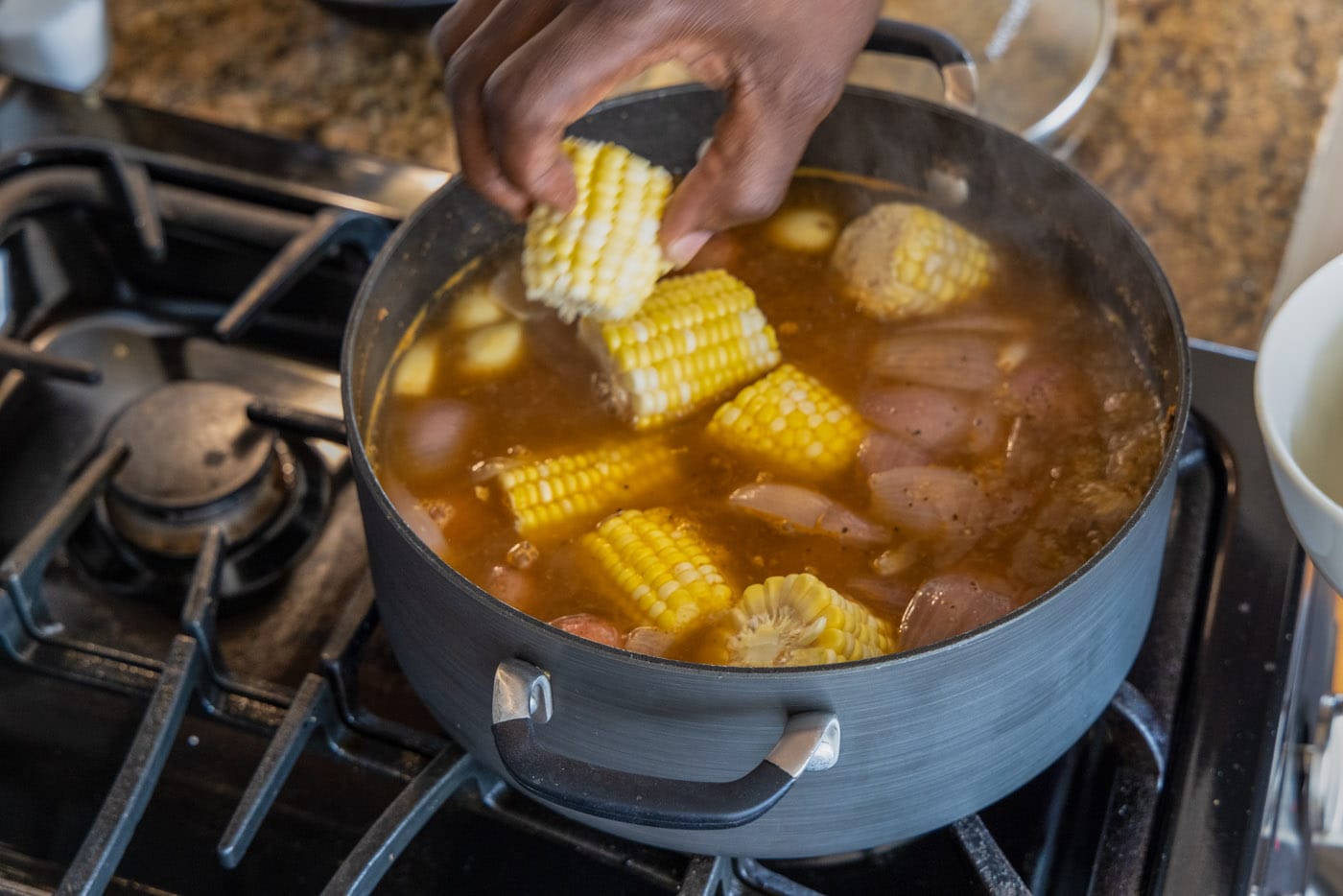 hand adding corn to shrimp boil pot