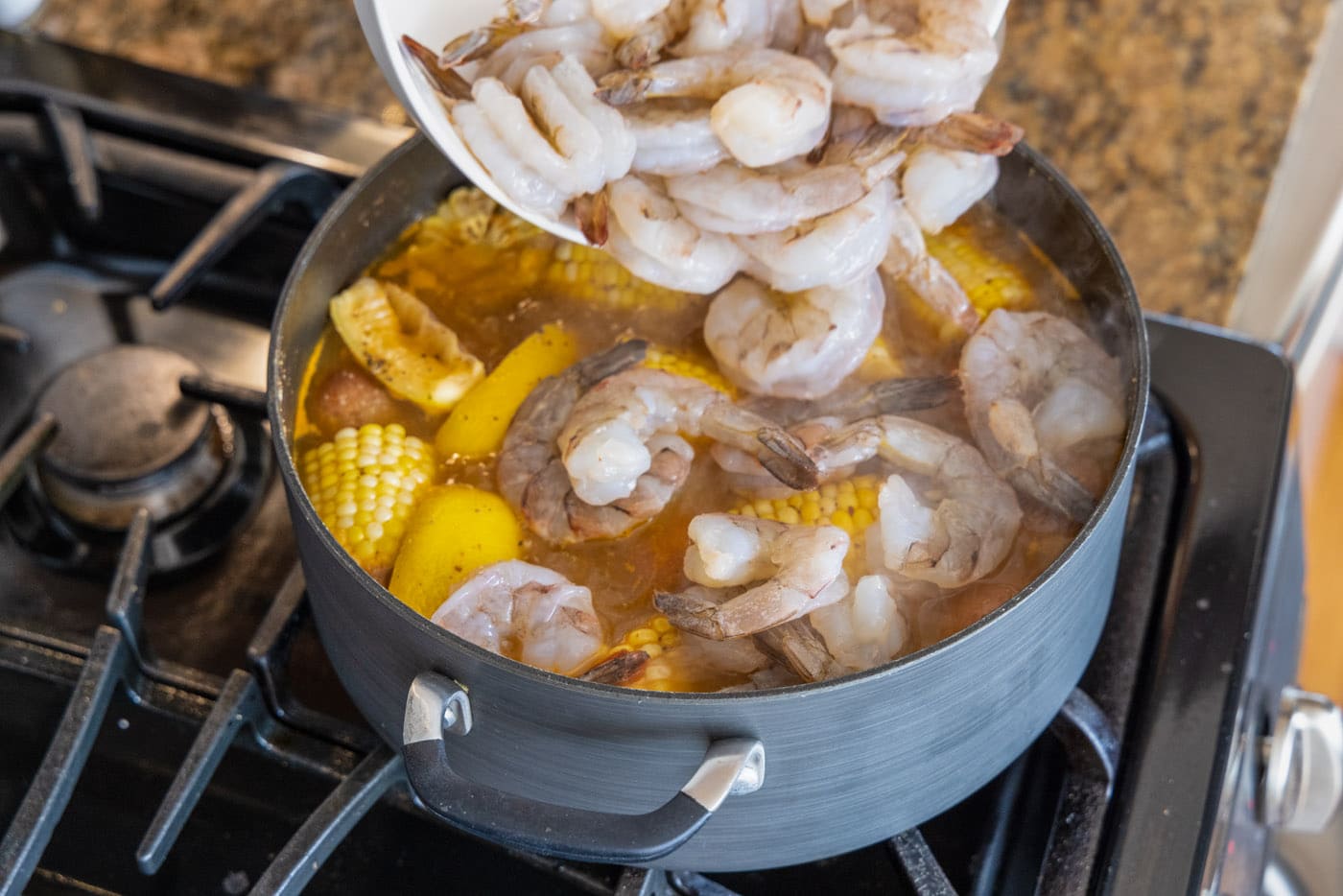 adding shrimp to large pot of shrimp boil