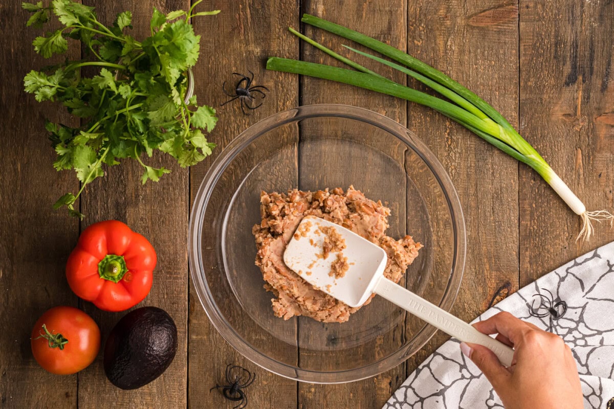 spreading refried beans on the bottom of a pie plate