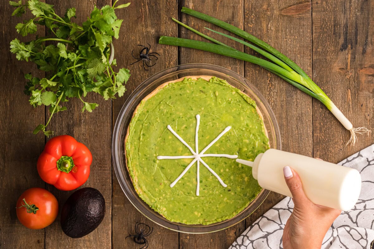 piping spiderweb design on top of guacamole