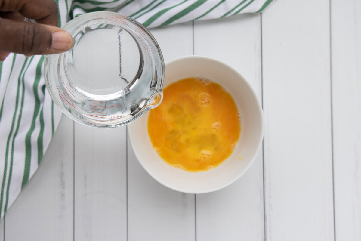 pouring water into eggs in a bowl
