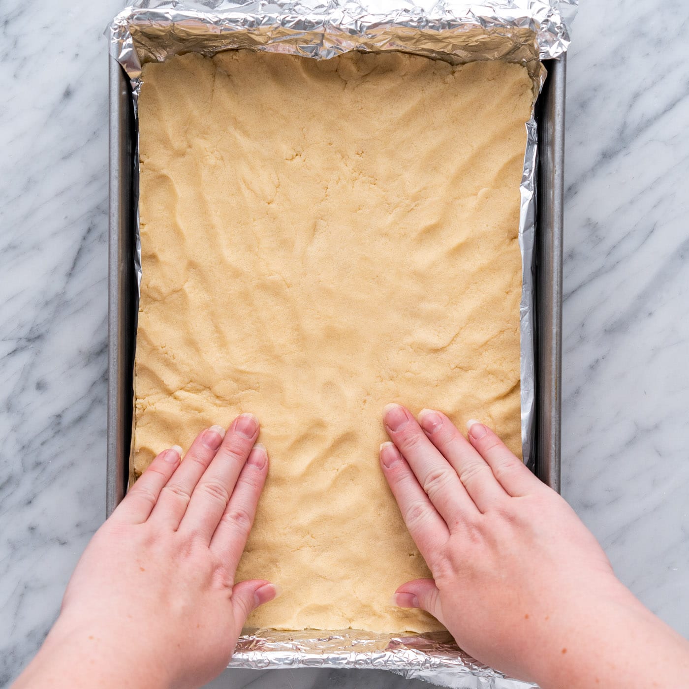 hands flattening shortbread crust in a baking pan