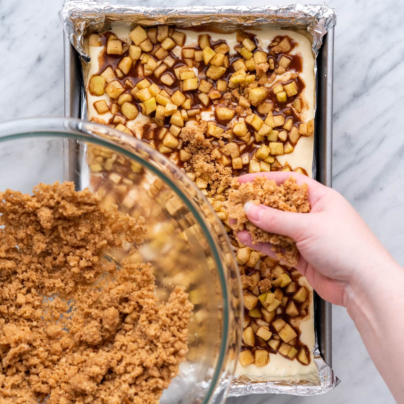 sprinkling streusel topping on top of caramel apple cheesecake bars