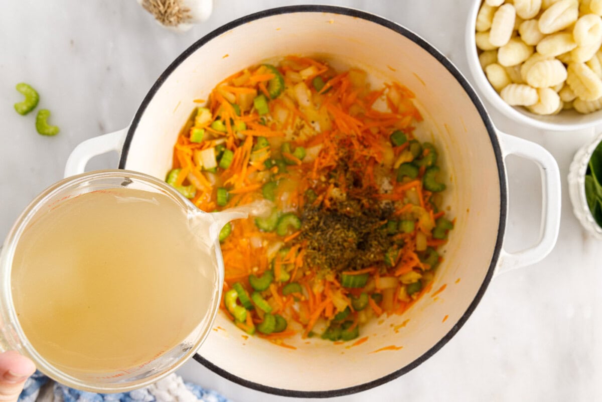pouring broth over vegetables in a pot
