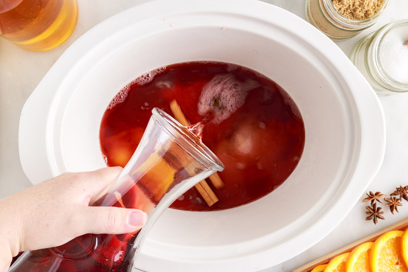 pouring juices into hot cranberry punch in the crockpot