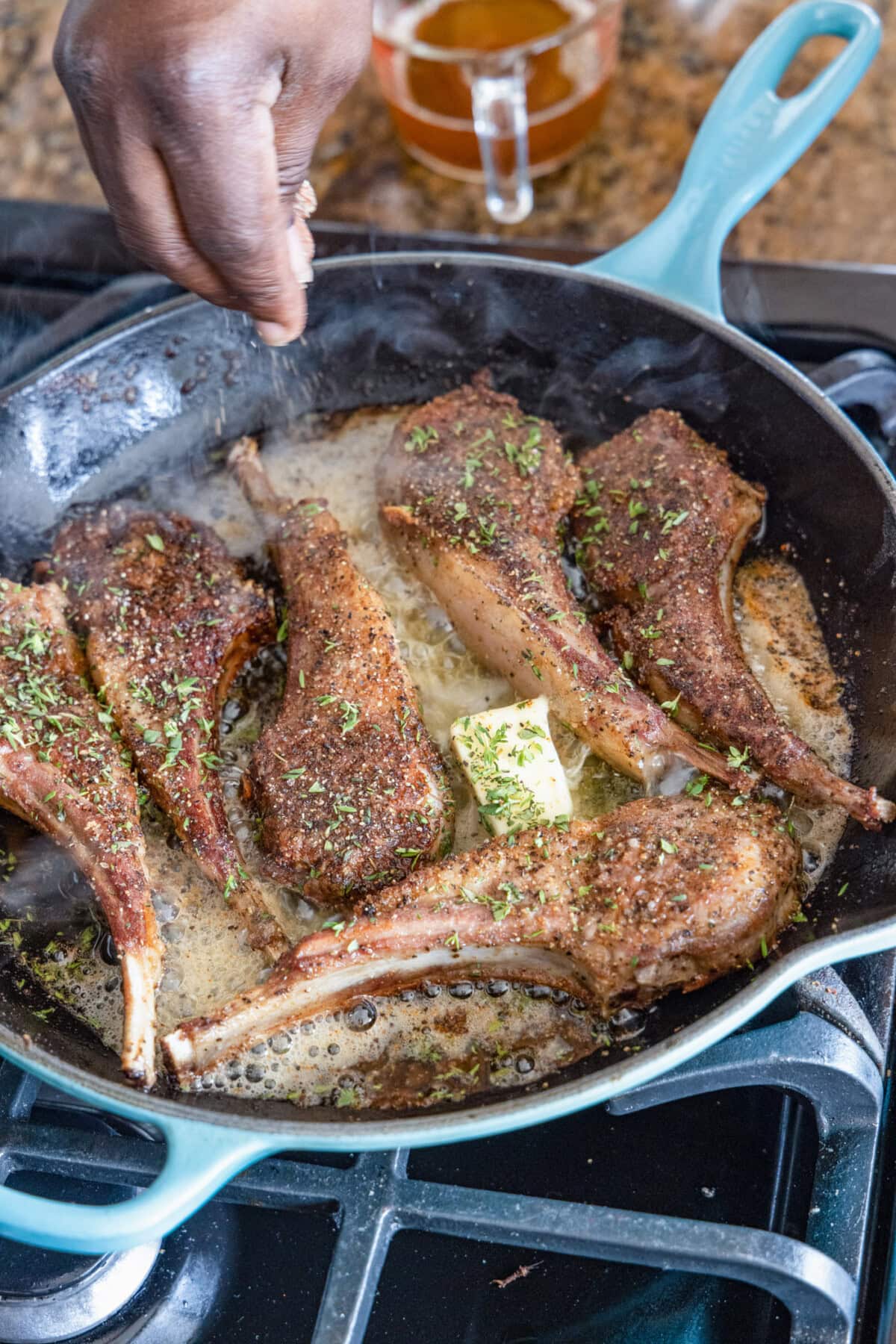 sprinkling thyme of Lollipop Lamb Chops in skillet