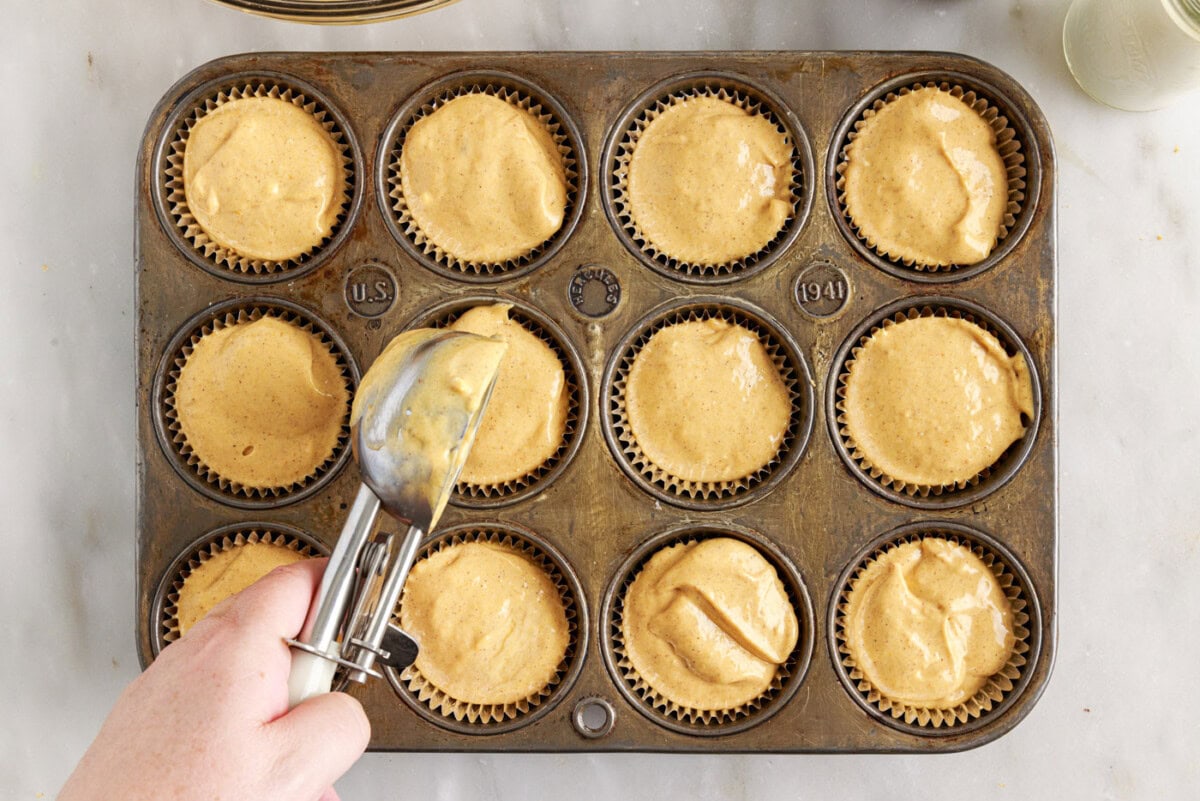 adding pumpkin cheesecake filling to a muffin tin