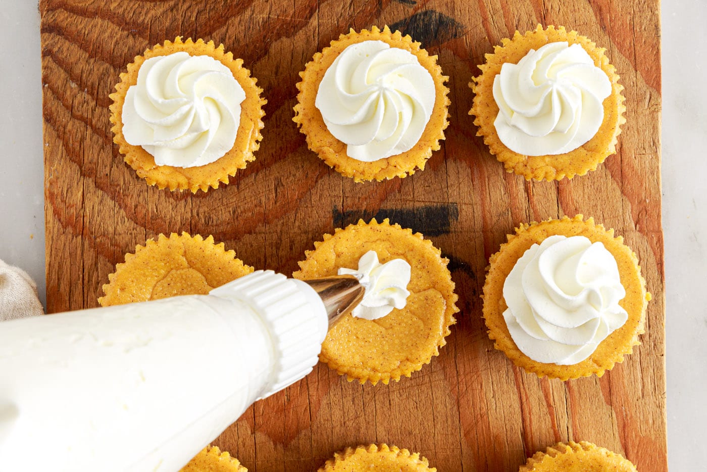 piping whipped cream on top of mini pumpkin cheesecakes