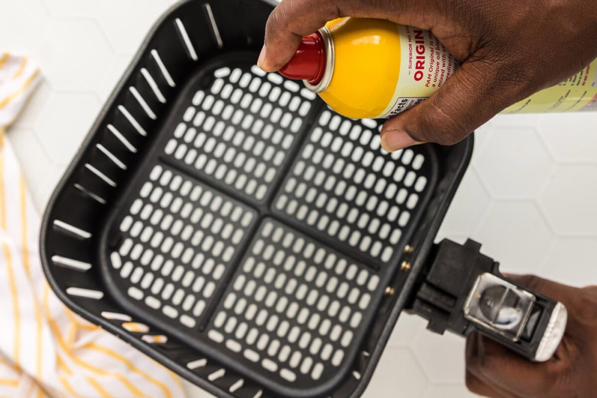 spraying air fryer basket with cooking spray