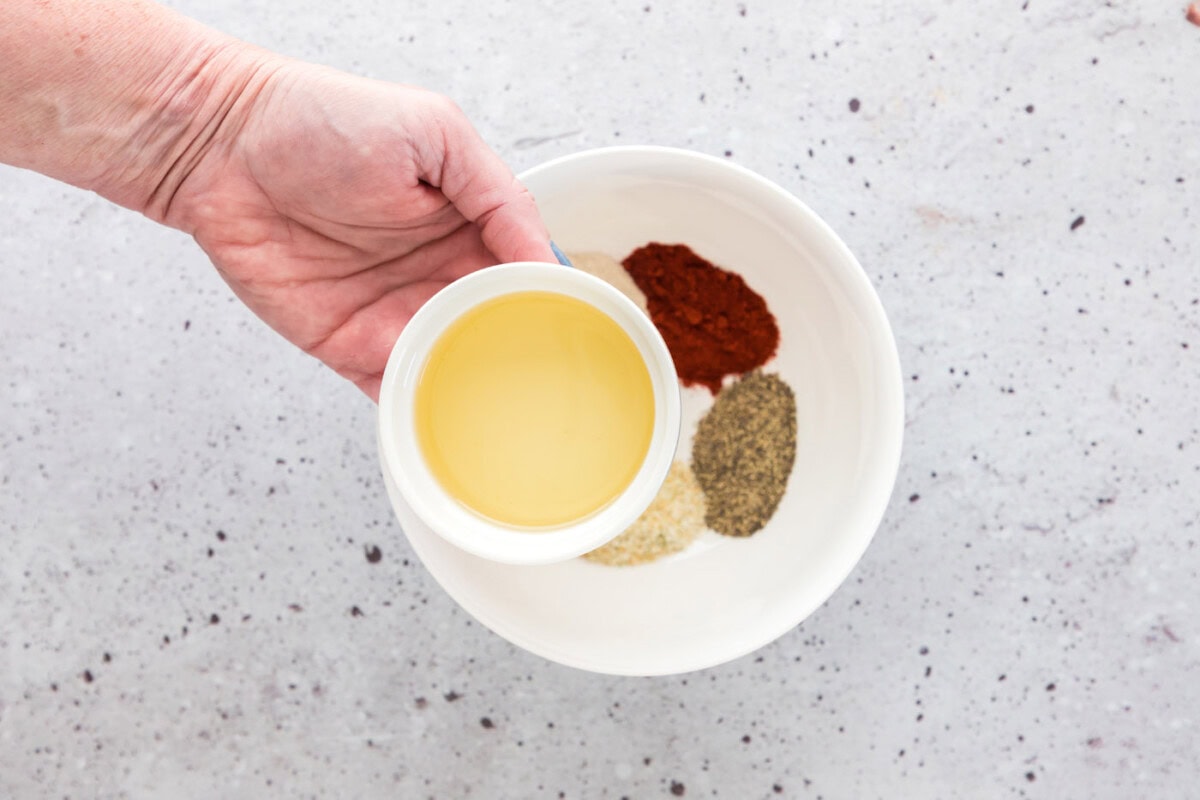 adding olive oil to seasoning mix in a bowl
