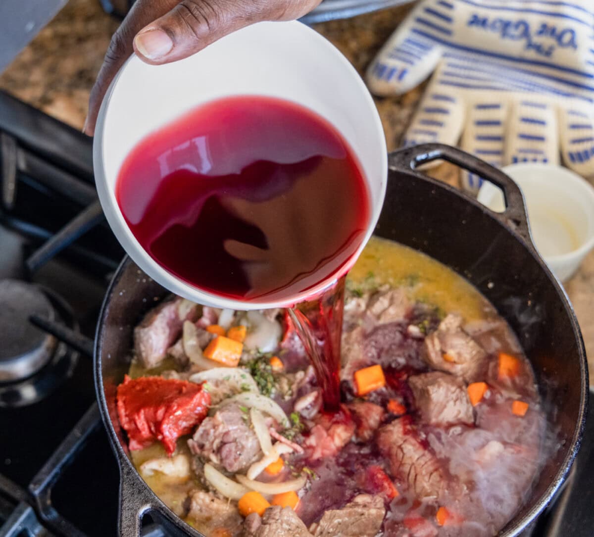 pouring red wine into beef bourguignon