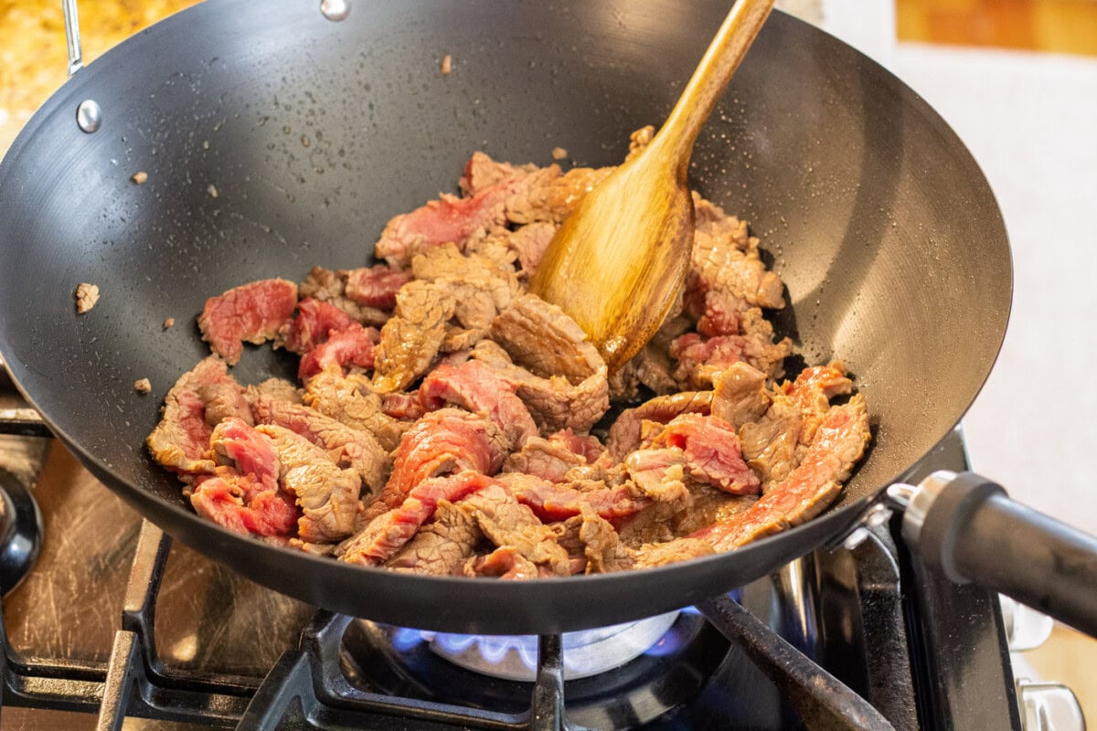 wooden spoon stirring sliced steak in a wok