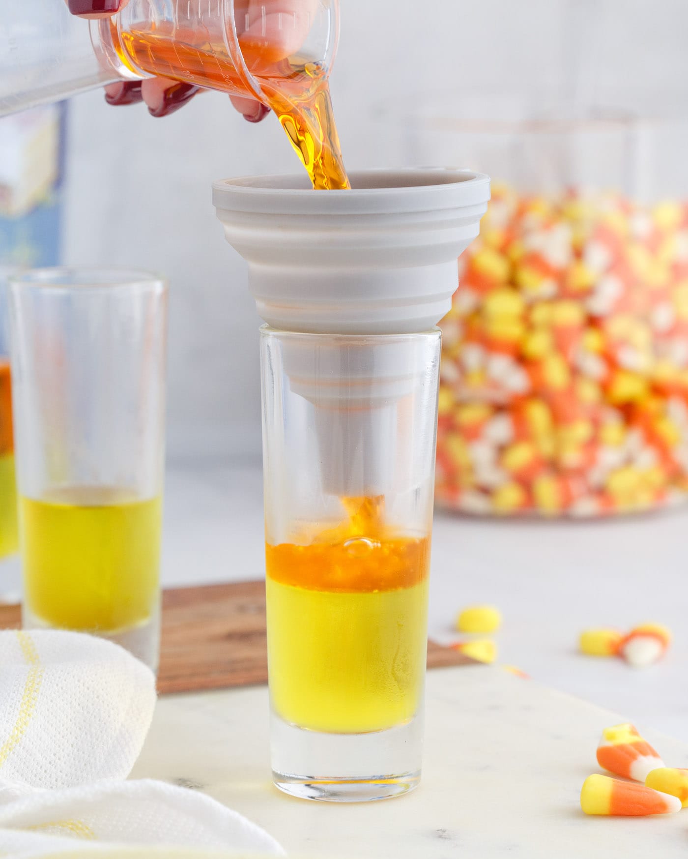 pouring orange jello mix over the top of lemon jello in a shot glass