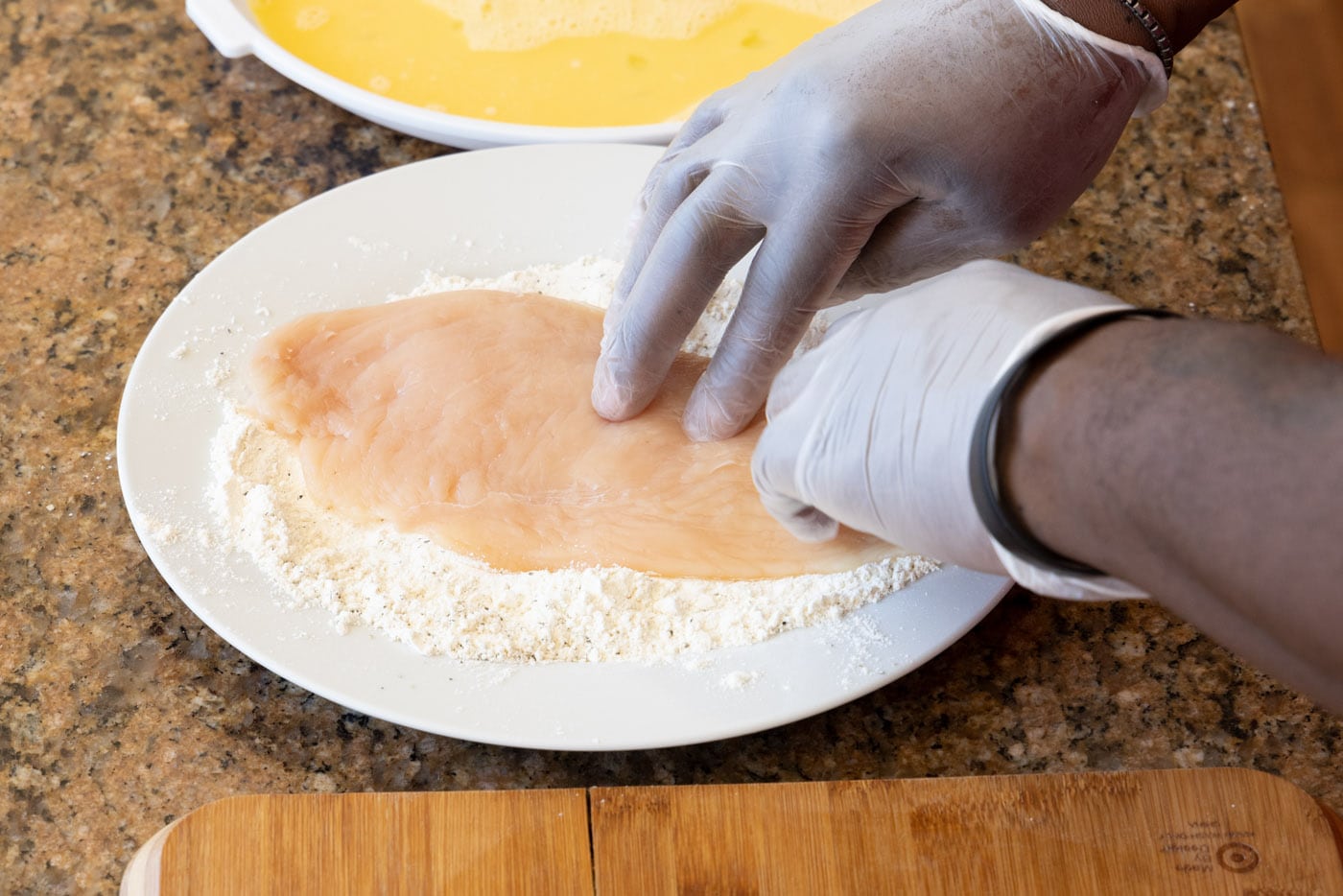 hand pressing chicken cutlet into flour