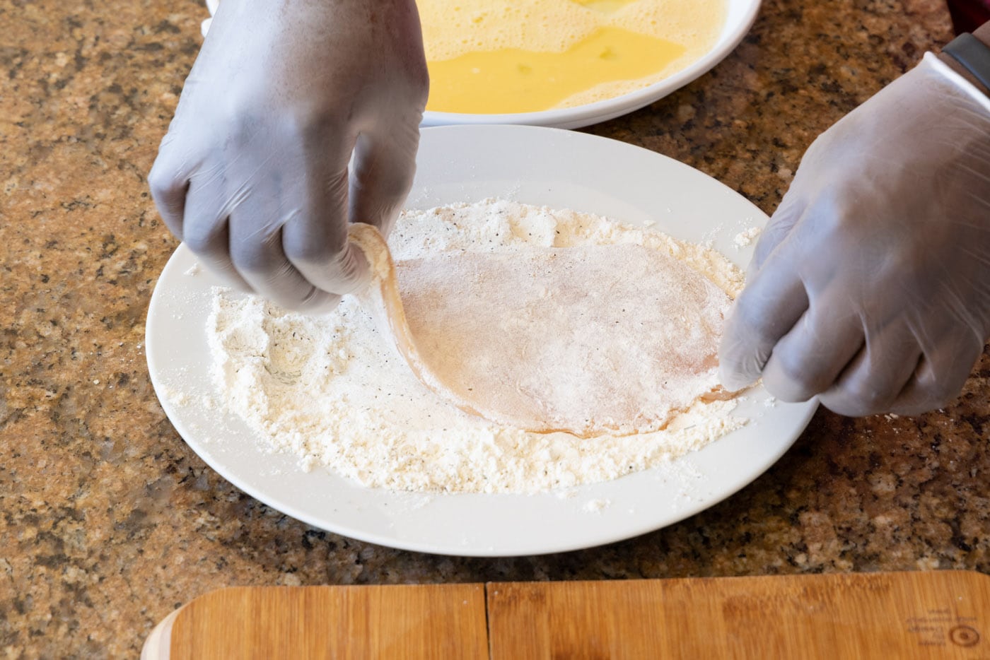 hand dredging chicken cutlet in flour