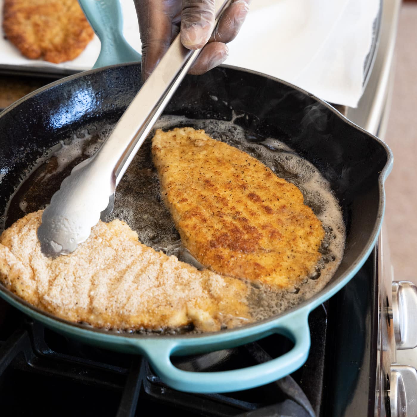 tongs flipping chicken cutlets in a skillet of oil