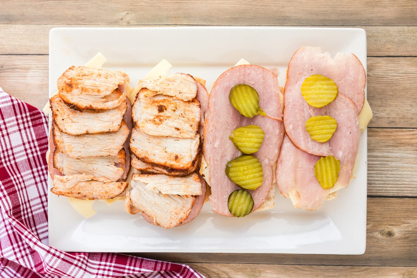 Pork tenderloin slices on top of cuban bread, ham, Swiss, and pickles