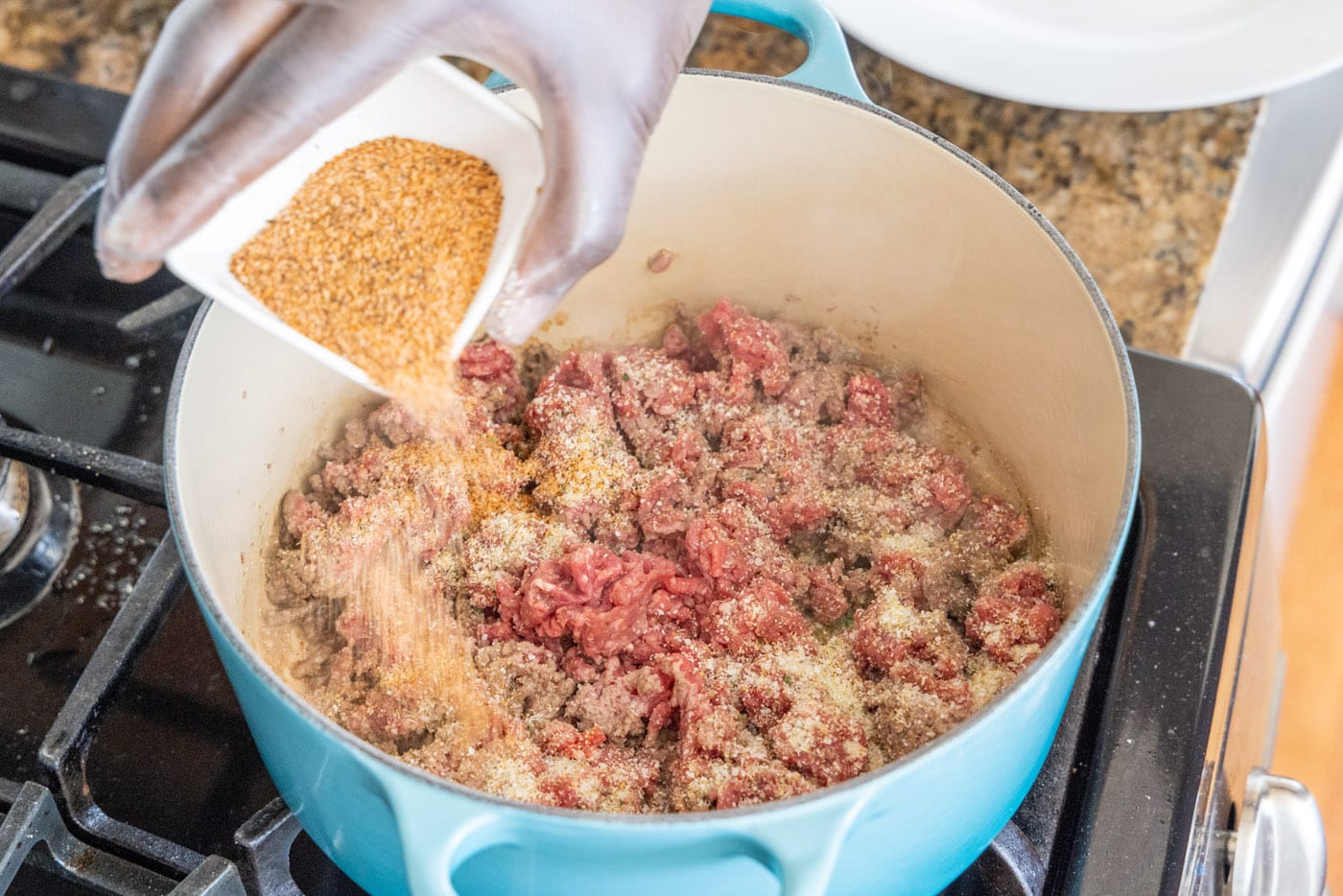 adding cajun seasoning to ground beef in a dutch oven