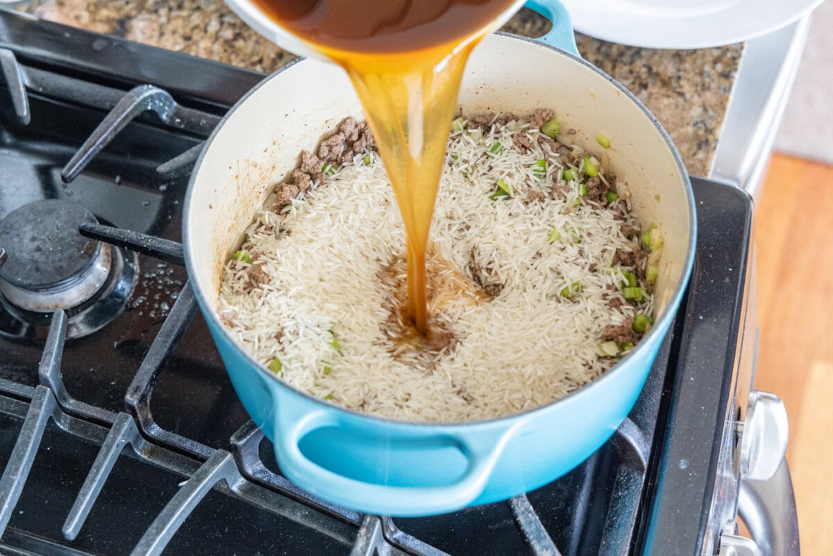 pouring beef broth over dirty rice