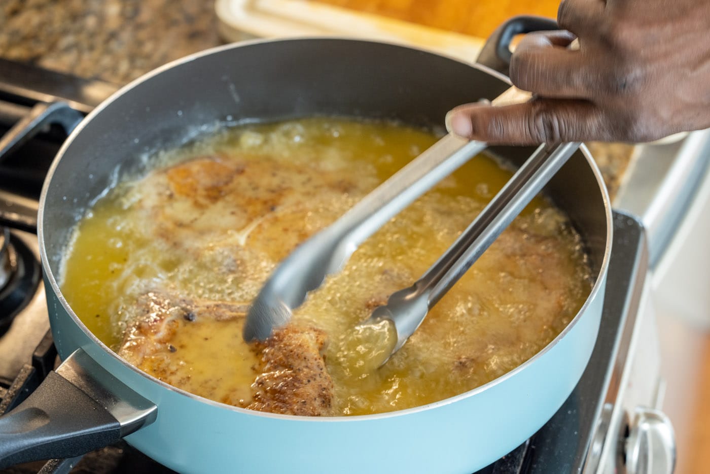 tongs flipping fried pork chops in a skillet